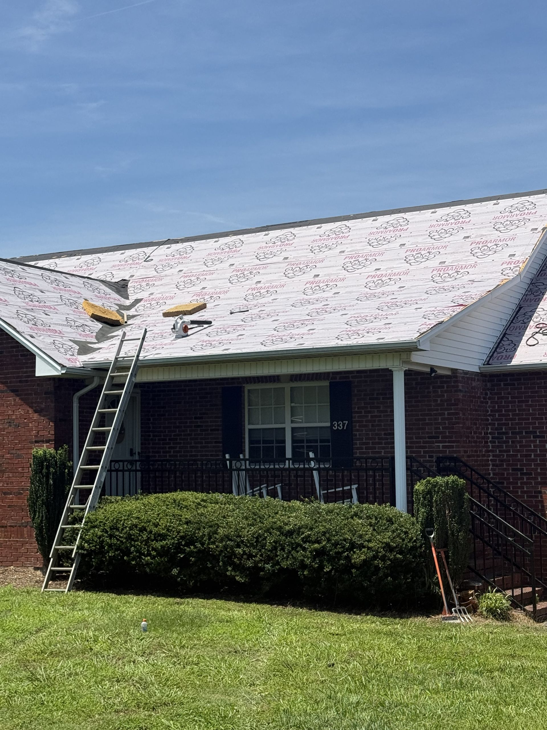 Brick house roof being repaired, with two workers on a ladder and white debris covering the shingles.