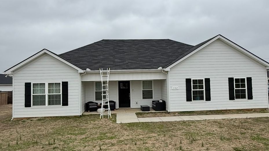 Single-story white house with black shutters, front porch, and a ladder leaning against the facade