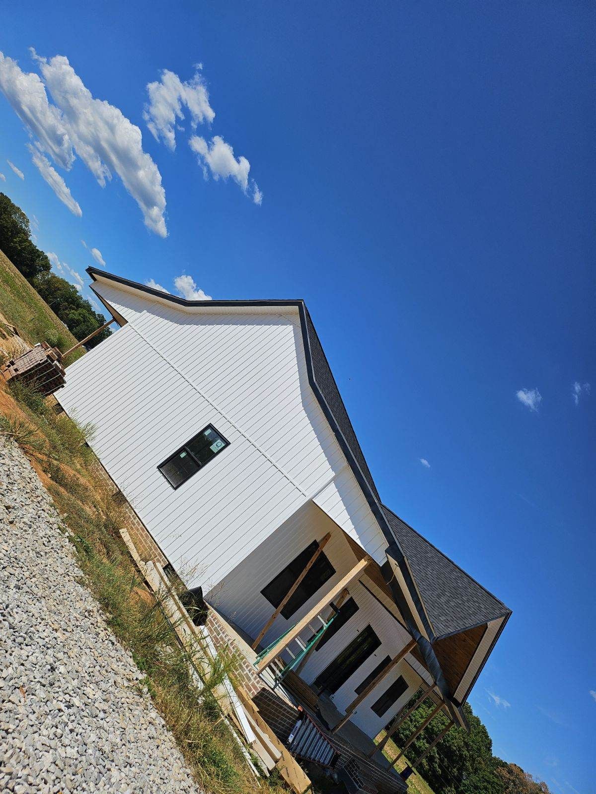 Tilted view of a white house with gray roof under a bright blue sky and scattered clouds