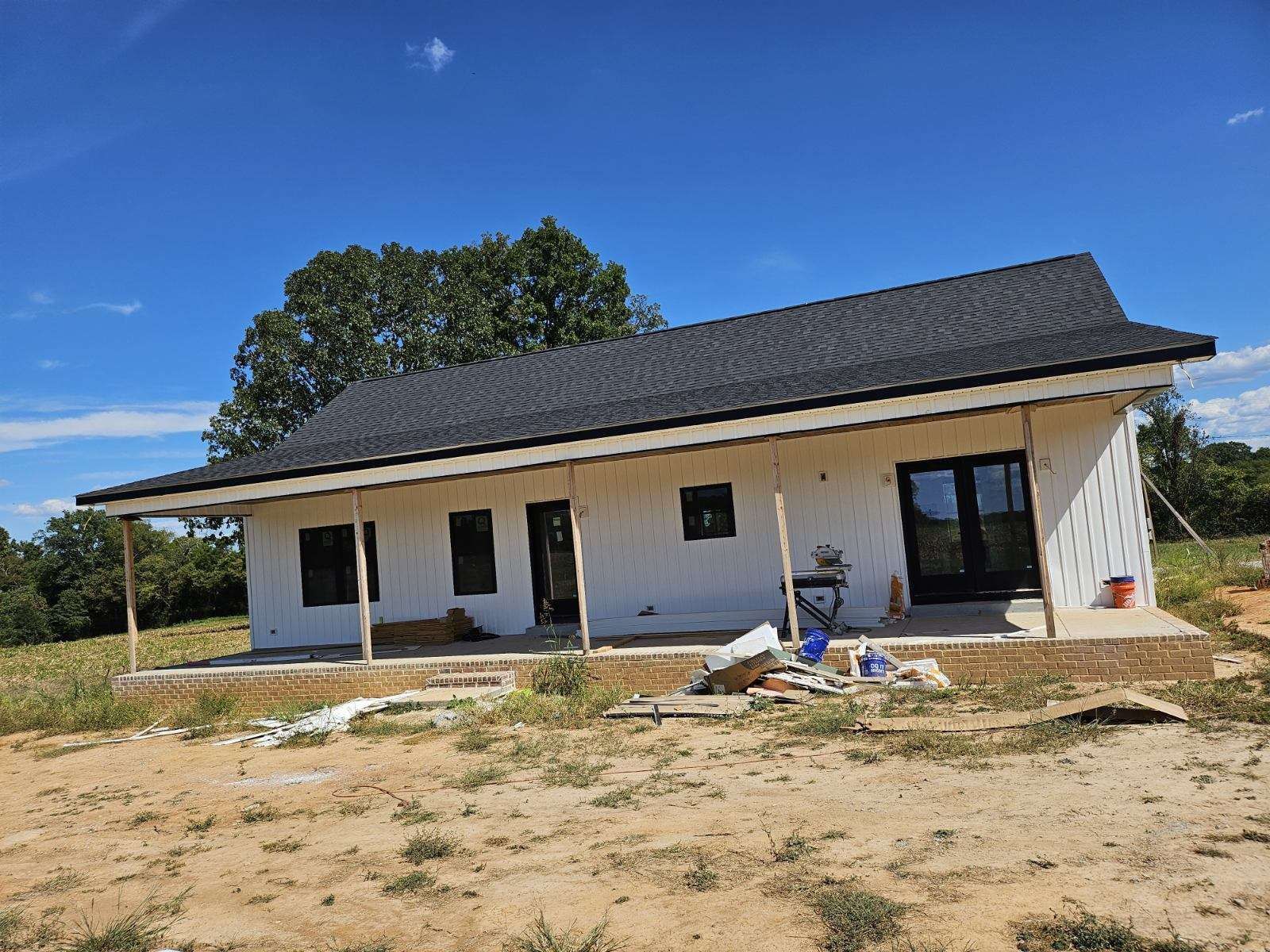 Small white house under construction with a dark roof on a sandy lot under a blue sky