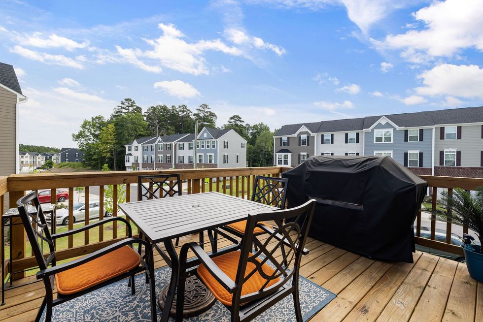 Patio deck with table, chairs, grill, and view of apartment buildings under a blue sky
