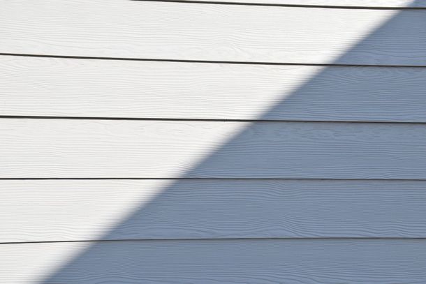 Diagonal shadow across white horizontal wooden siding in sunlight