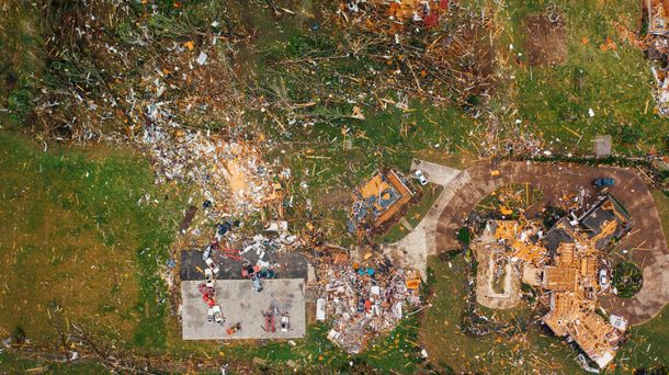 Aerial view of a crowded outdoor construction or disaster site with rubble, debris, and damaged buildings.