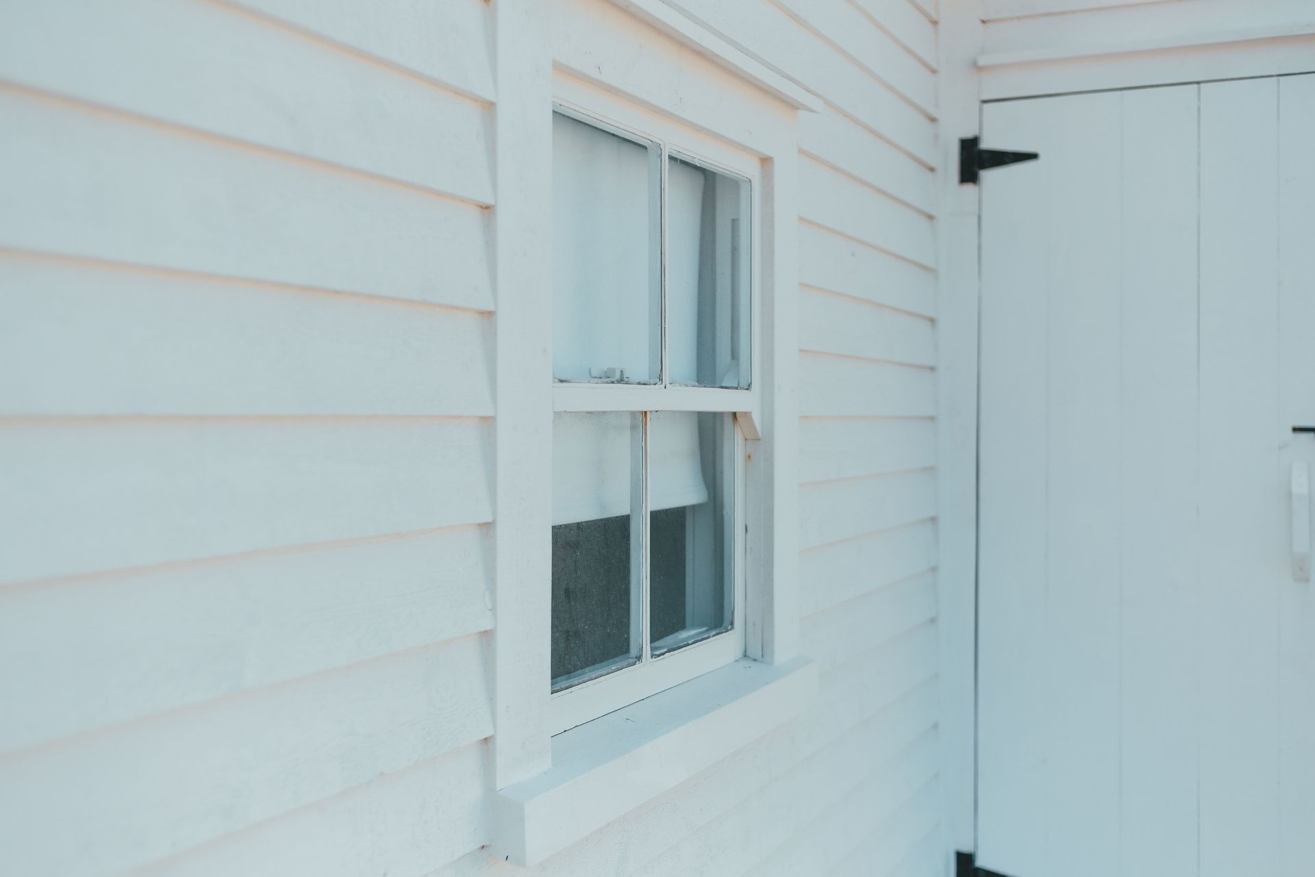 White house exterior with a window beside a white door and black hinge.