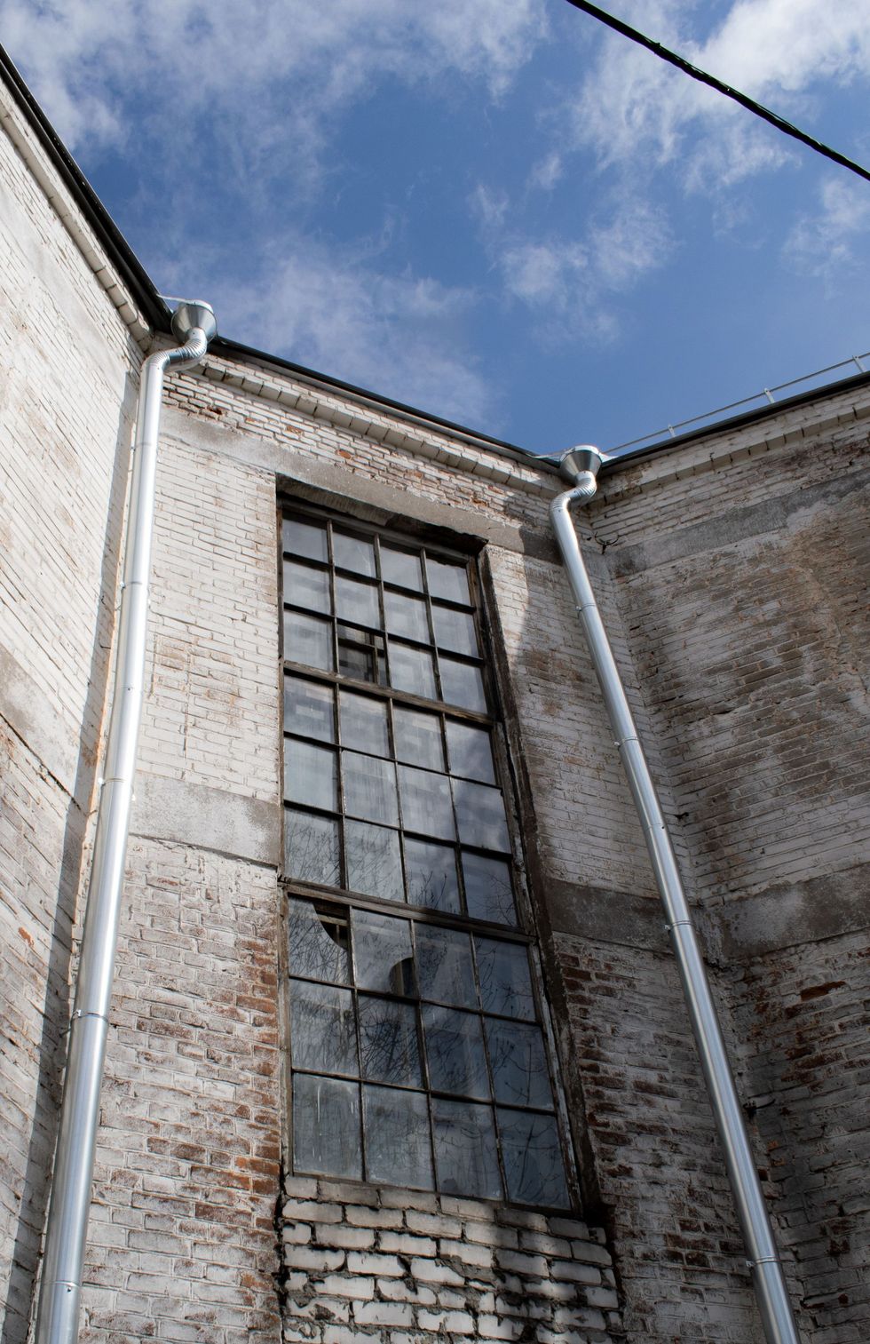Tall dirty window on a brick industrial building against a blue sky