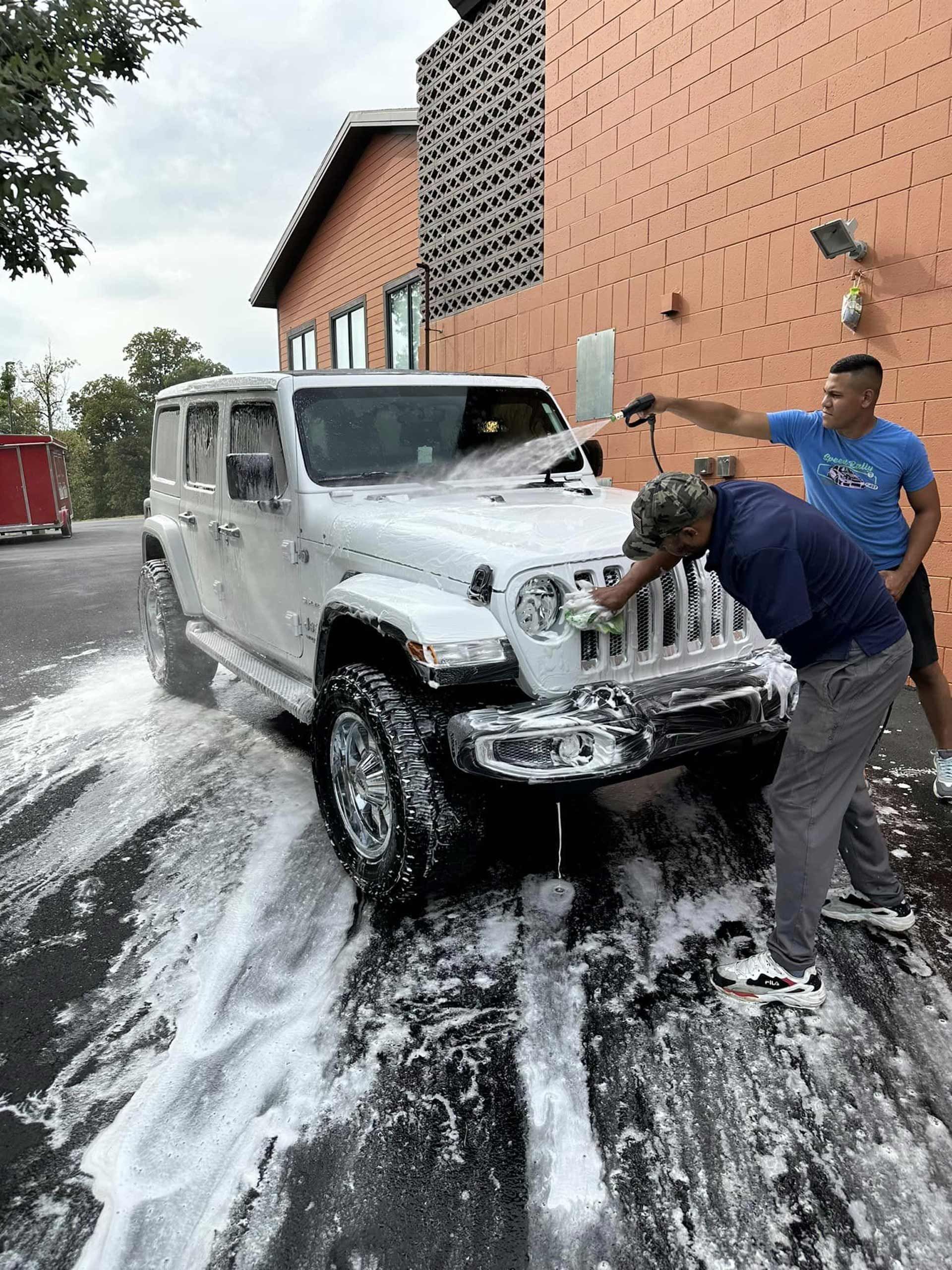 Two men are washing a white jeep in front of a building