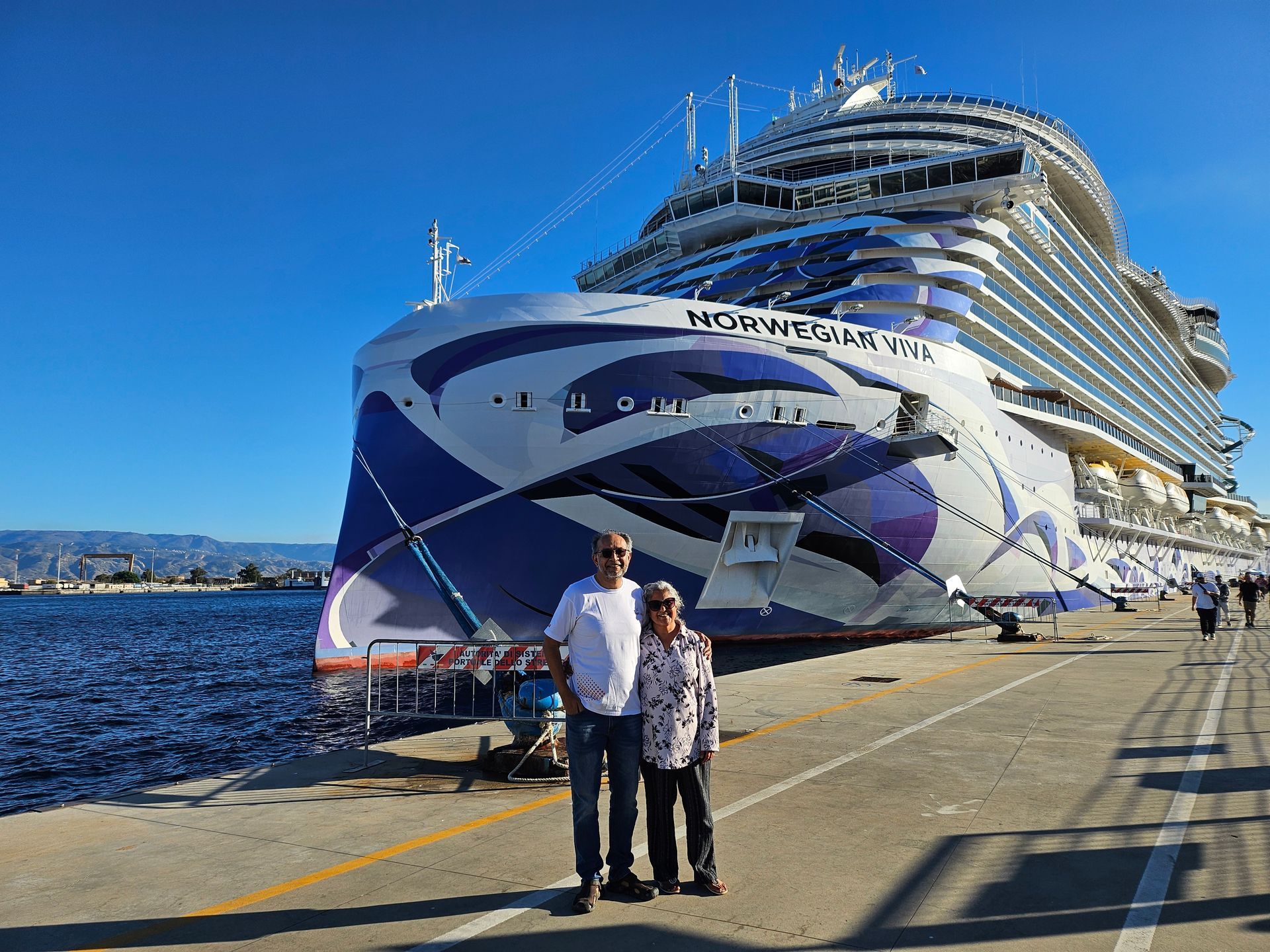 Couple poses in front of the Norwegian Viva cruise ship on a sunny day.