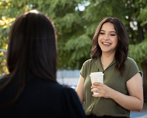 a woman is holding a cup of coffee and smiling while talking to another woman .