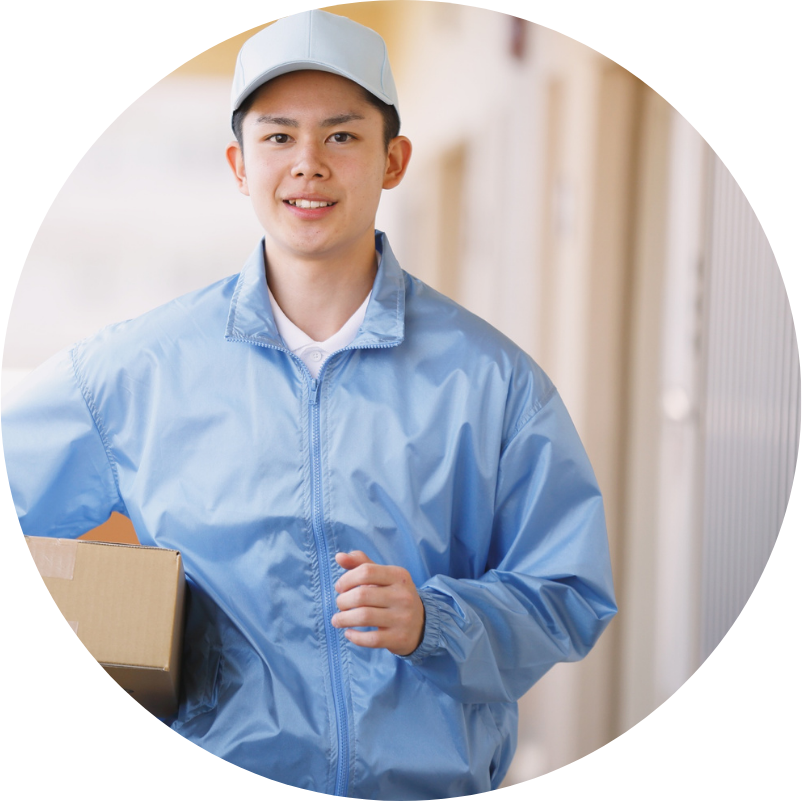 Delivery person in blue uniform, carrying a package, smiling outdoors.