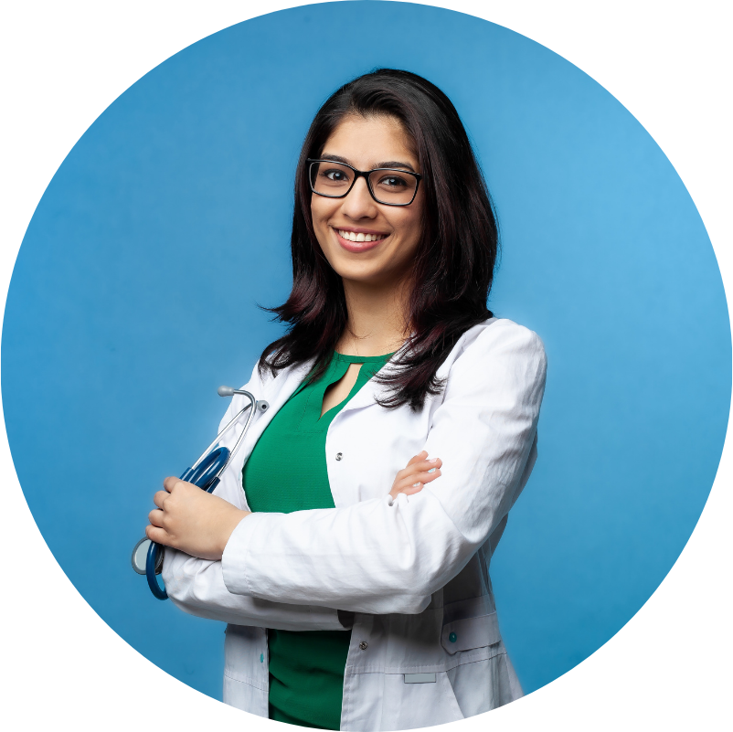 Smiling doctor with glasses, arms crossed, wearing a white coat, green shirt, and stethoscope. Blue background.