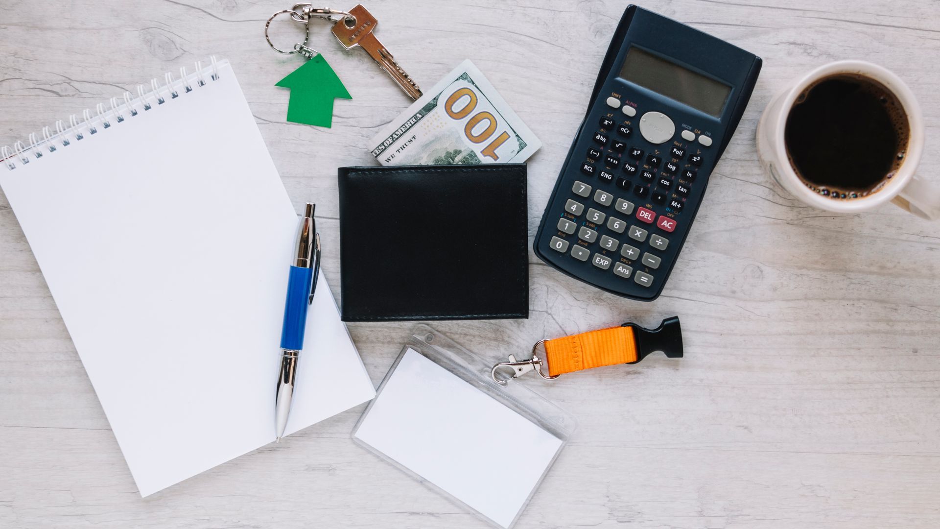 A calculator , wallet , pen , keys , and a cup of coffee are on a table.