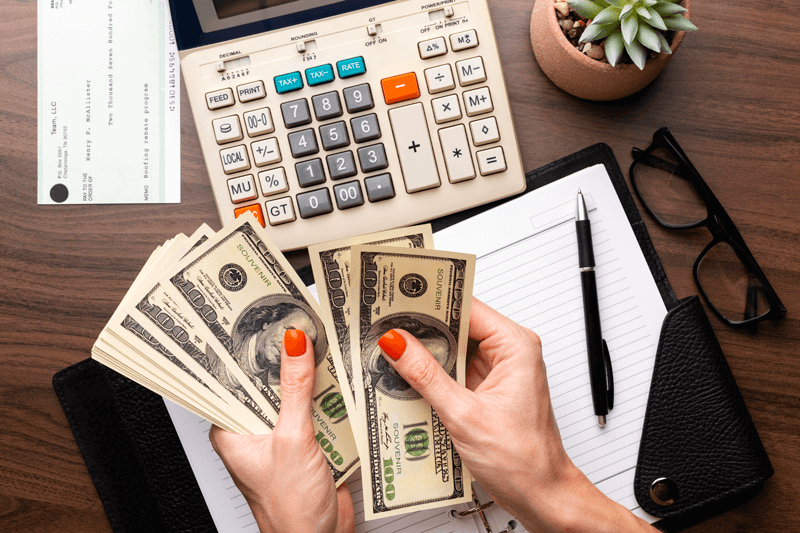 A woman is holding a stack of money in front of a calculator.