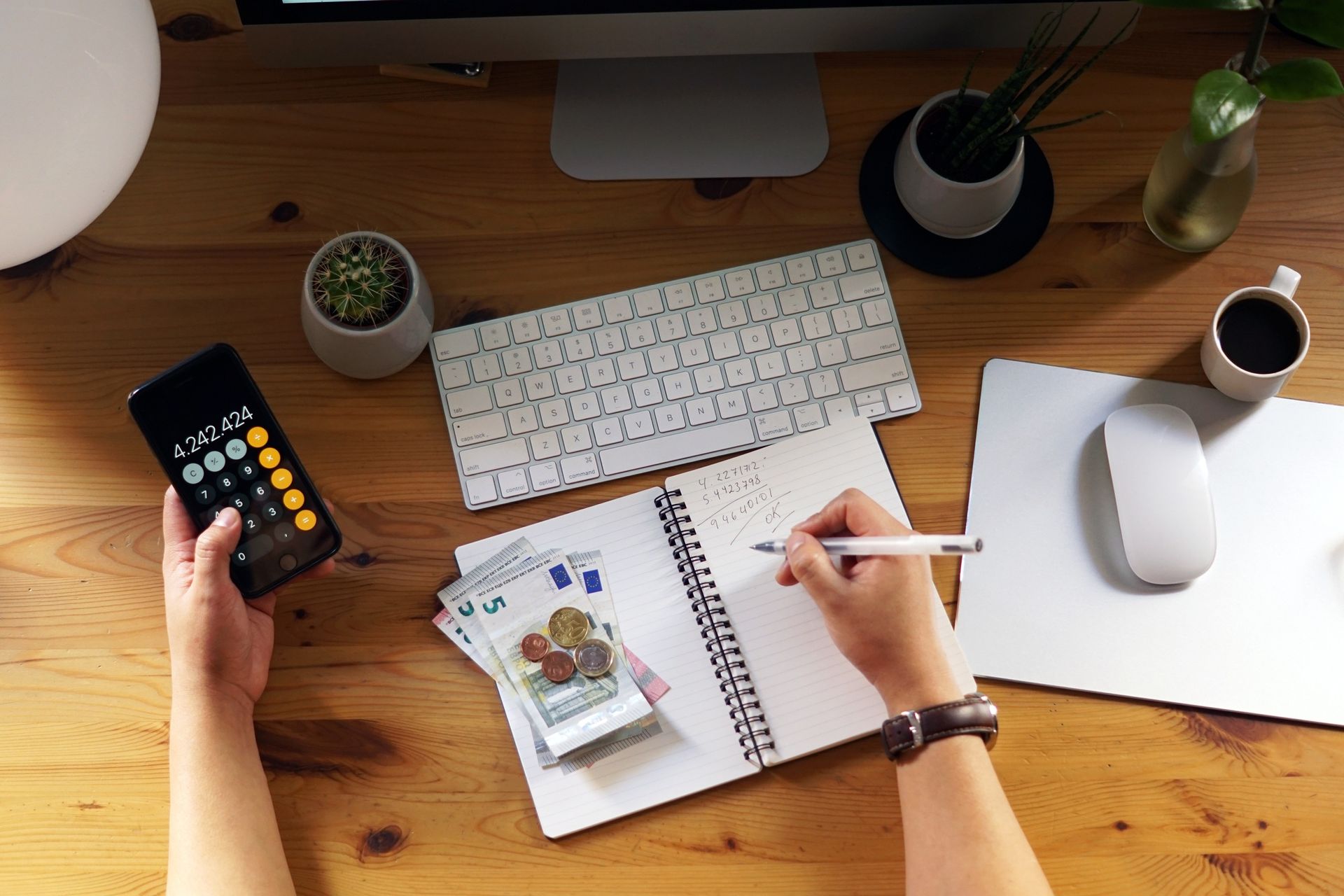 A person is sitting at a desk using a calculator and writing in a notebook.