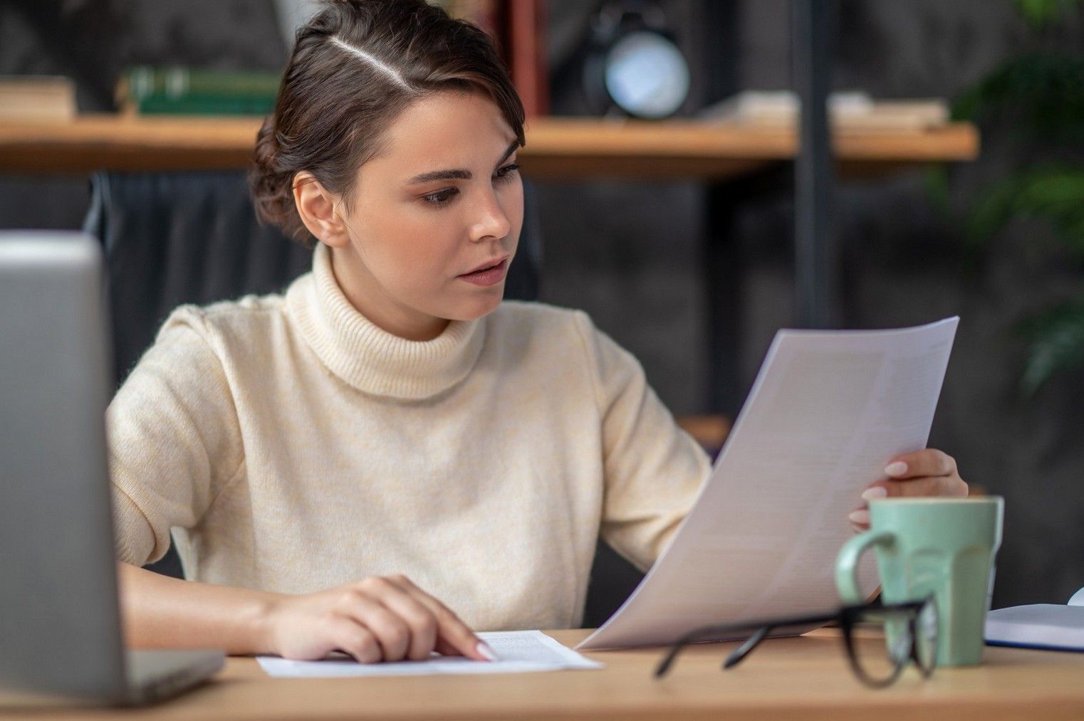 A woman is sitting at a desk looking at a piece of paper.