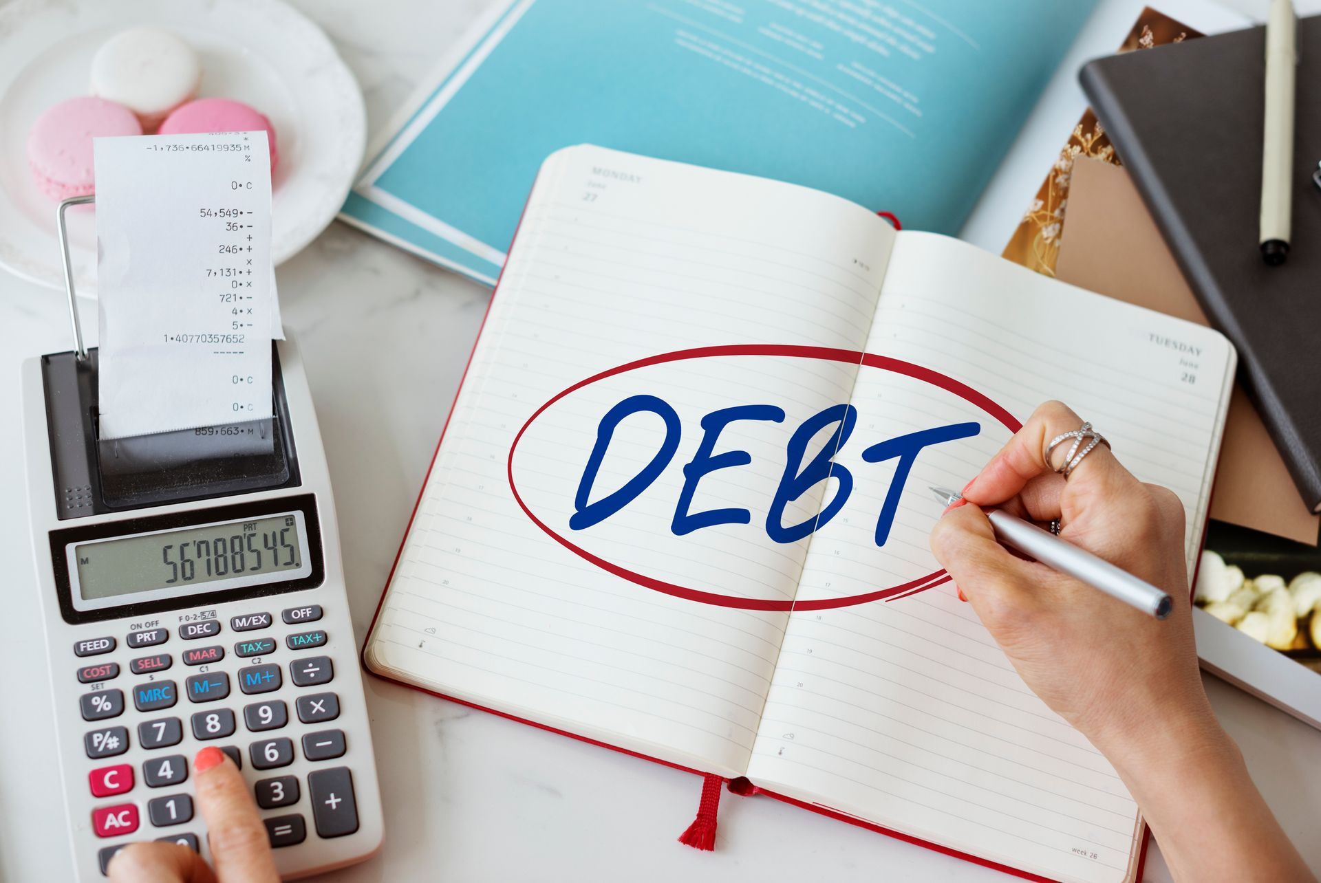 A person is writing the word debt in a notebook next to a calculator.