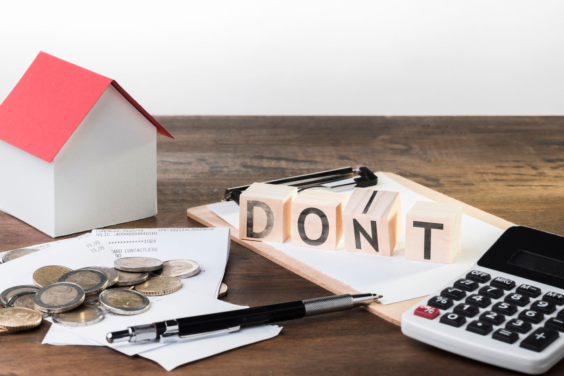 A wooden table with a house , coins , a pen , a calculator and blocks that say do n't