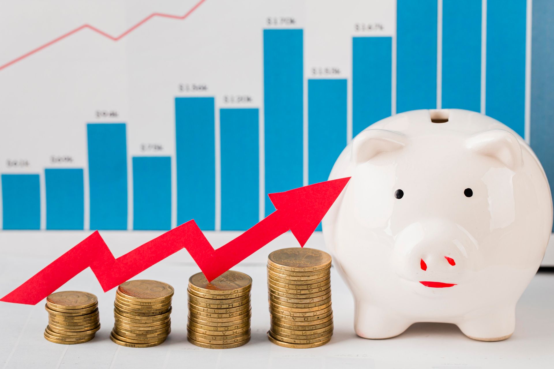 A piggy bank sitting next to stacks of coins with a red arrow pointing up.