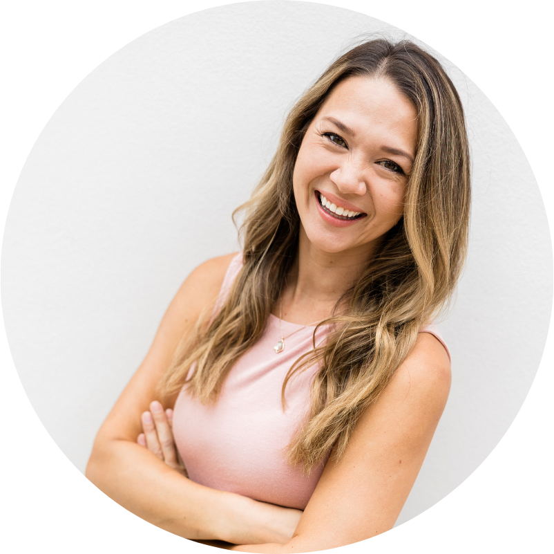 Woman with long wavy hair, smiling, arms crossed, wearing a pink top, against a white background.