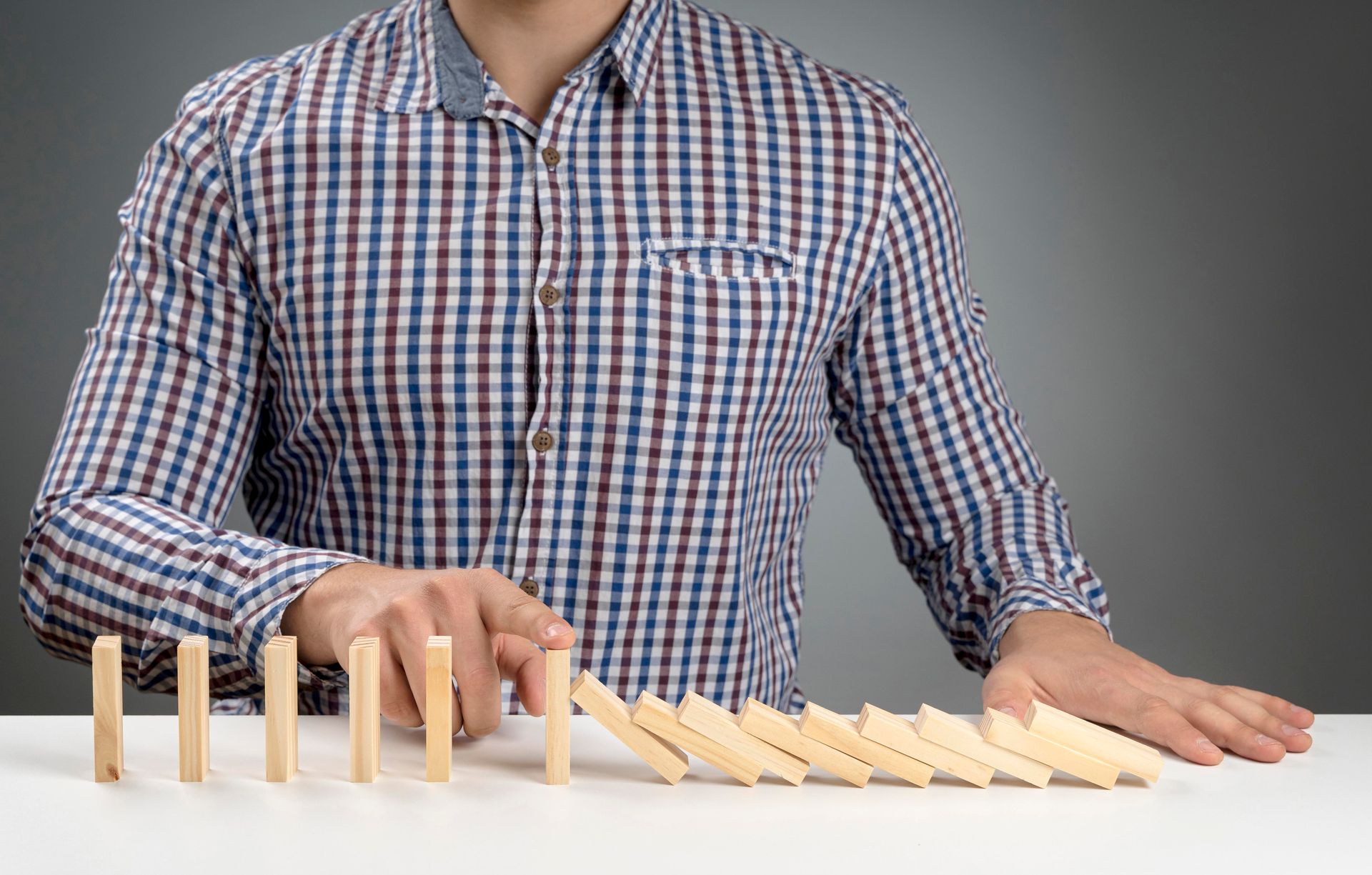 A man in a plaid shirt is playing with dominoes on a table.