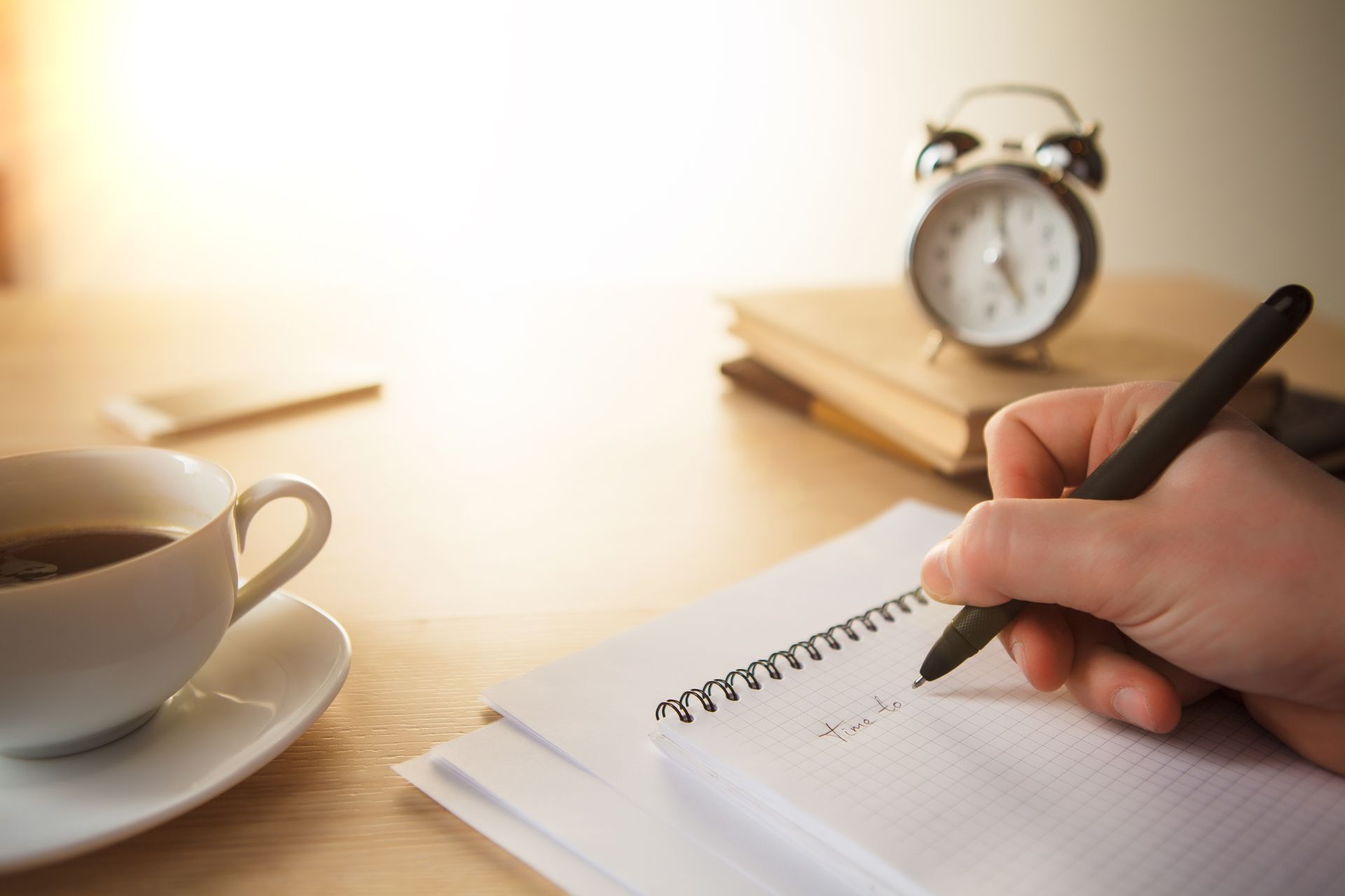 A person is writing in a notebook next to a cup of coffee.