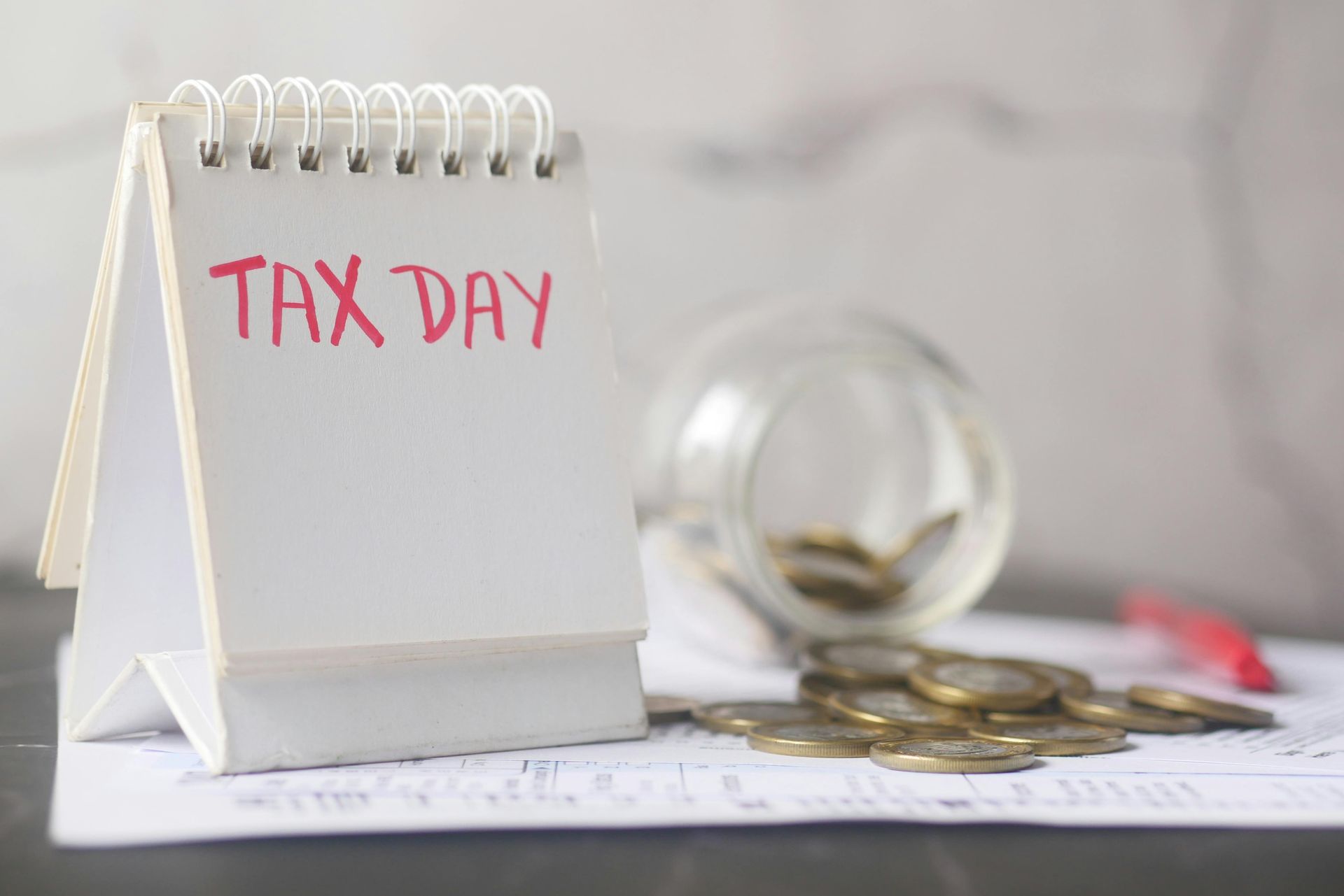Desk calendar labeled “TAX DAY” beside coins and a calculator on papers