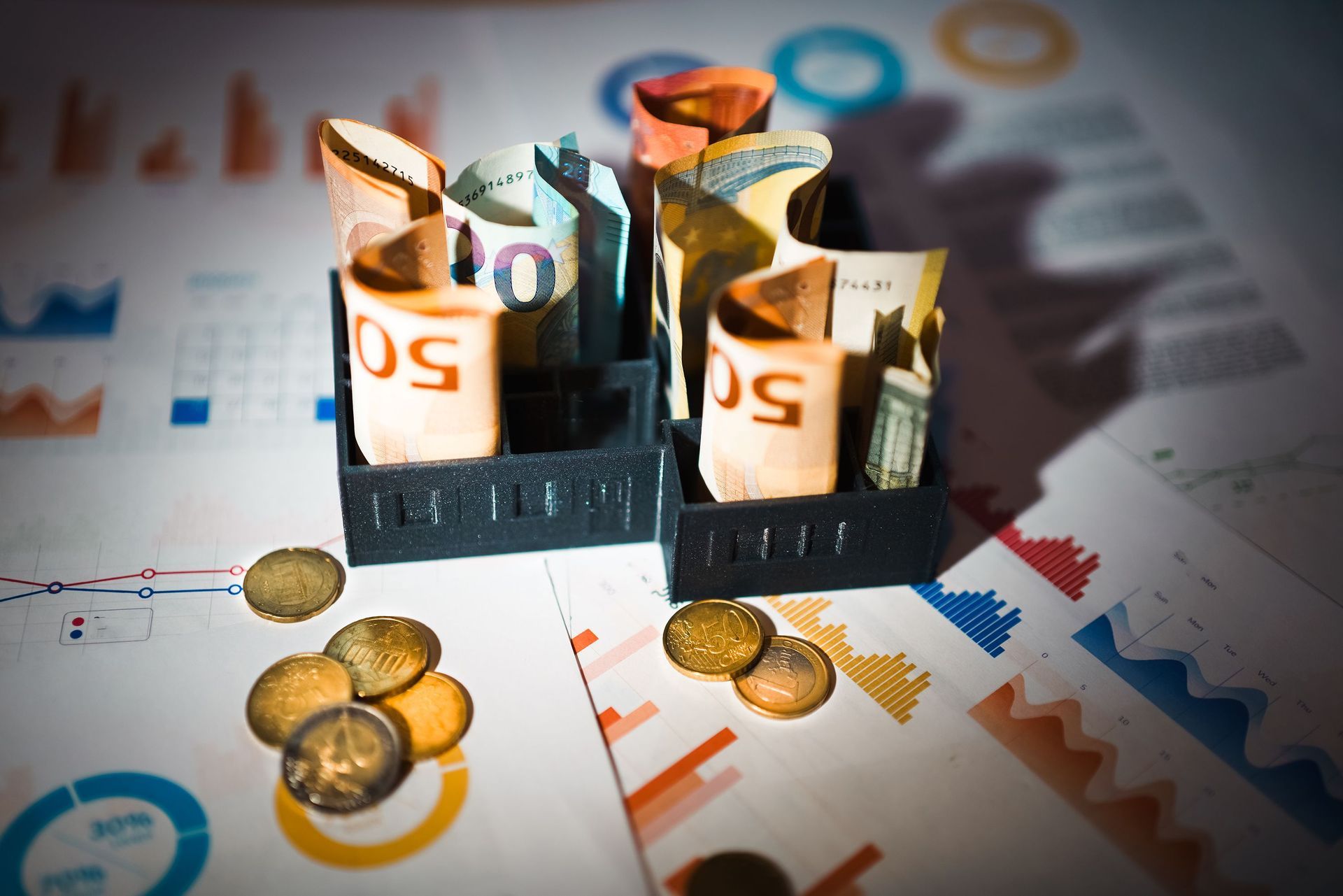 Coins and rolled banknotes in black trays on financial charts and graphs