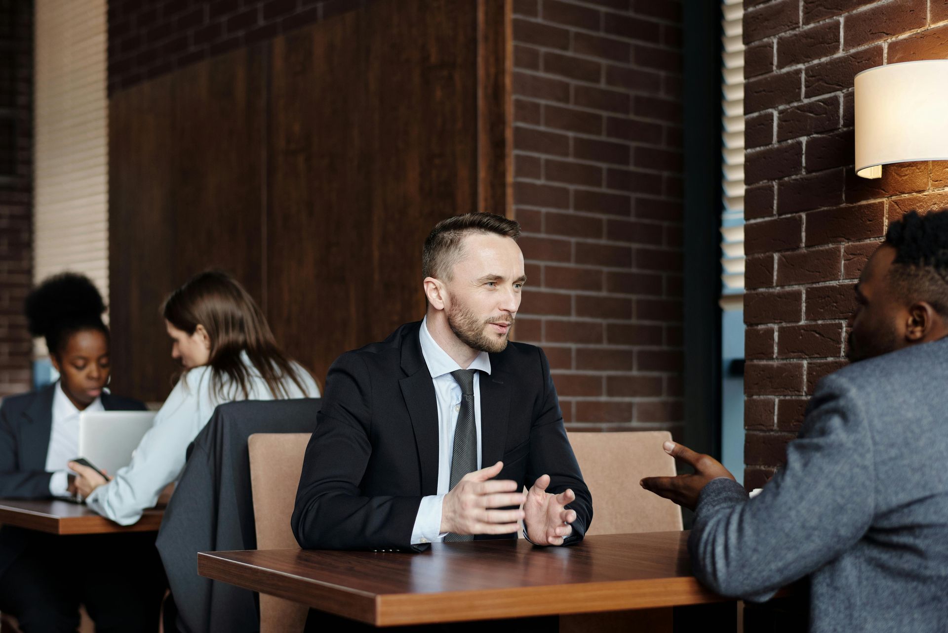 two women are sitting at a table with a laptop and talking .