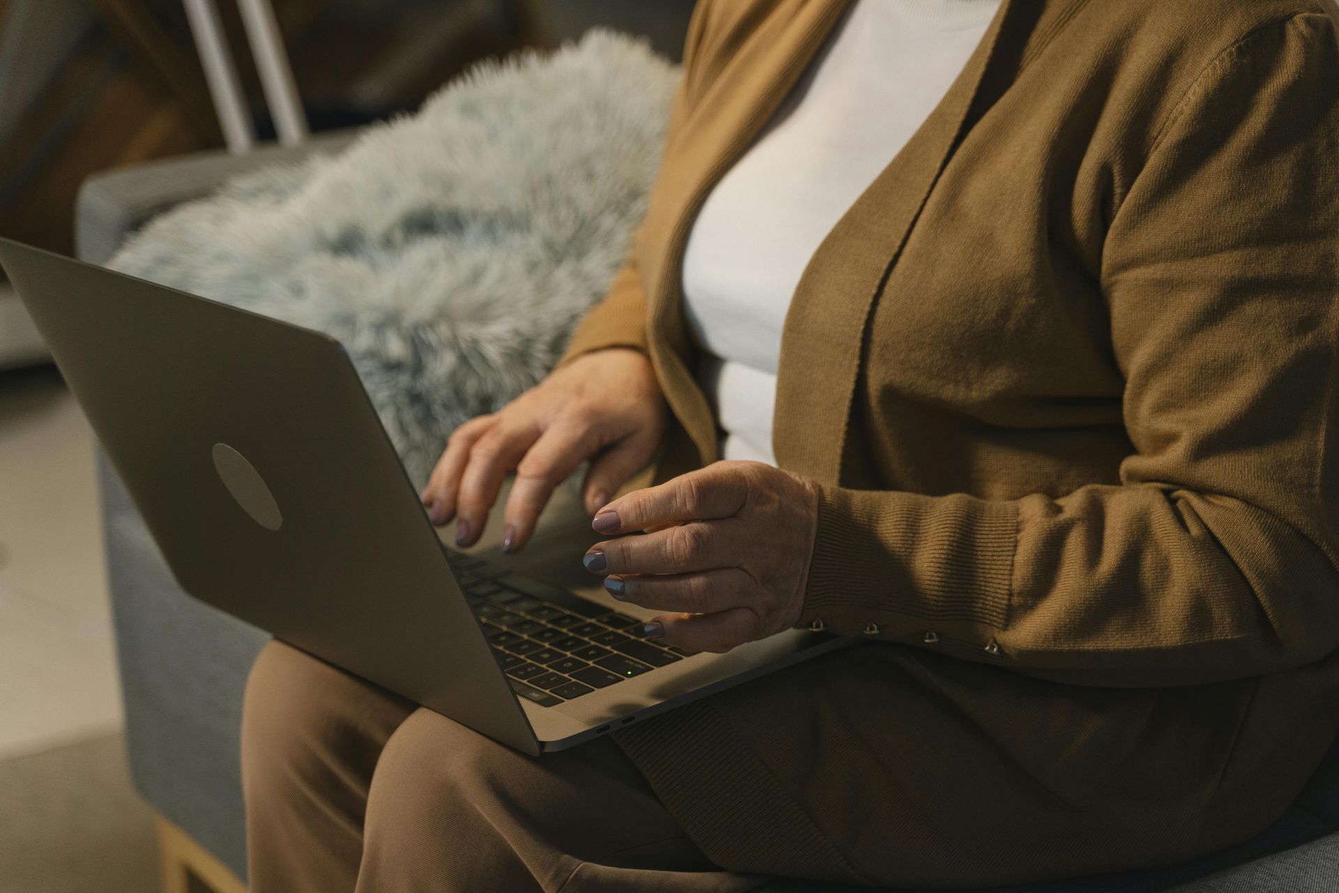 Person using a laptop, seated, wearing a brown cardigan and white shirt.