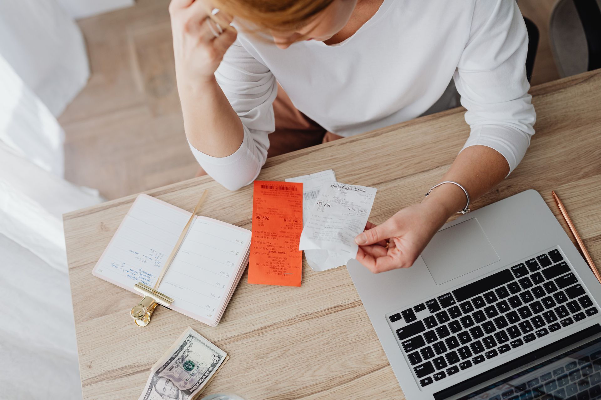 Person at a desk with laptop, notebook, cash, and a bright orange note, appearing to review finances