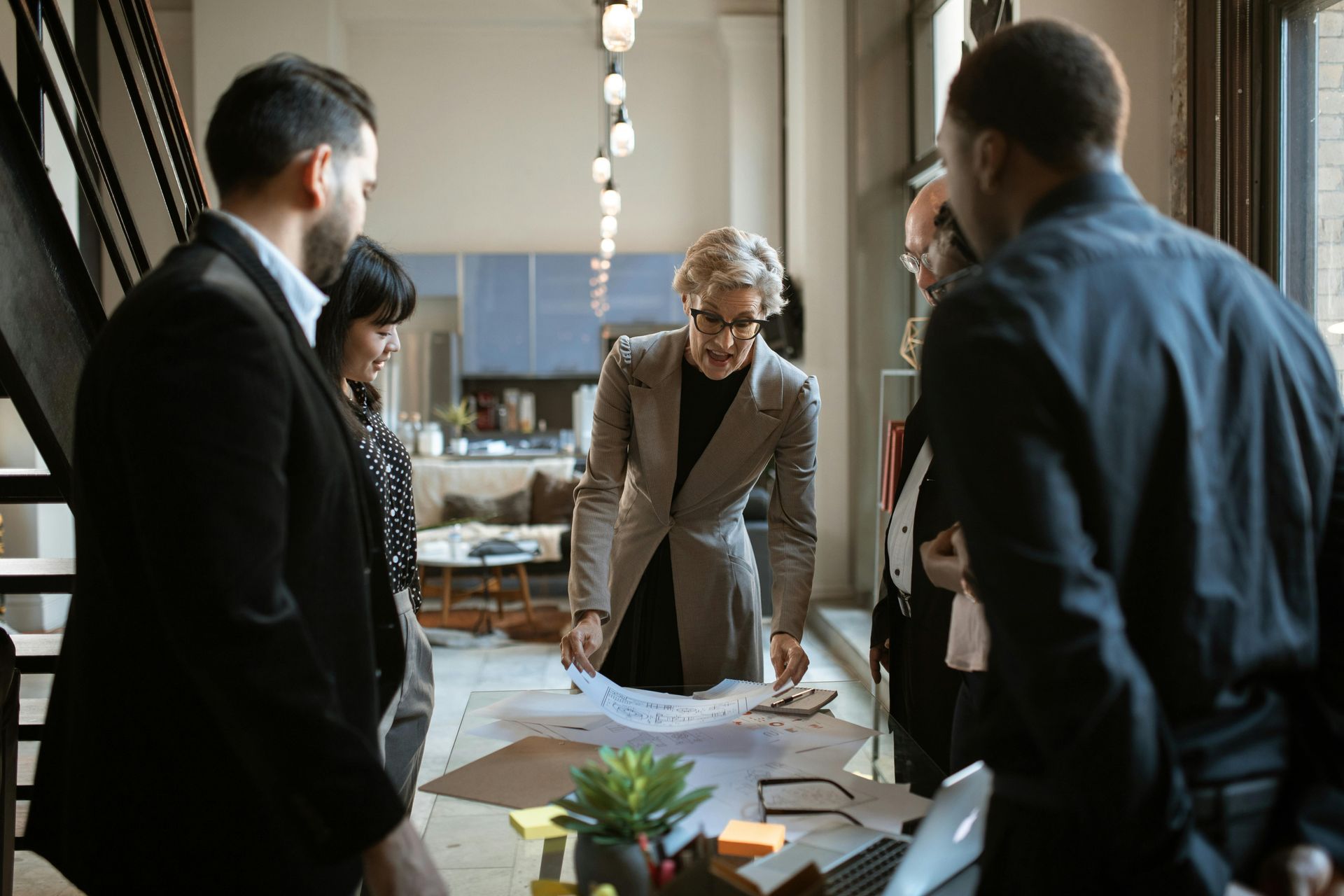 Businesspeople in a bright office, gathered around a table examining a blueprint.