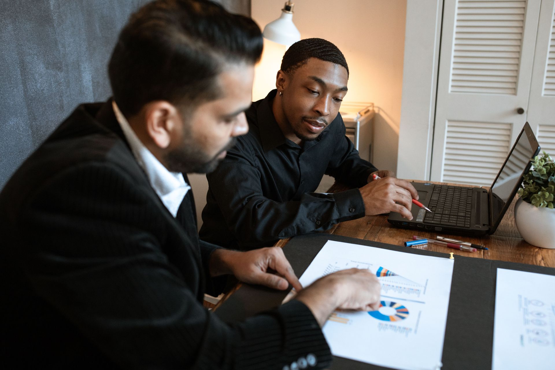 Two coworkers reviewing charts and a laptop at a desk in a meeting room