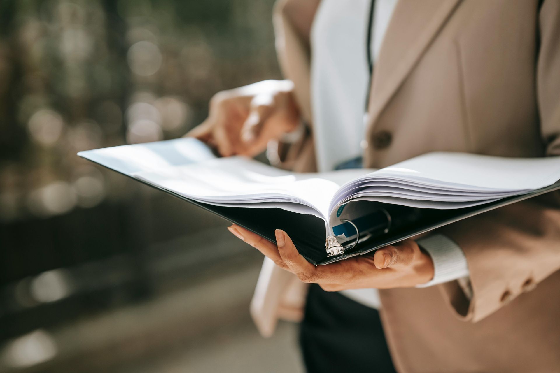 A woman in a suit is holding a binder with papers in it.