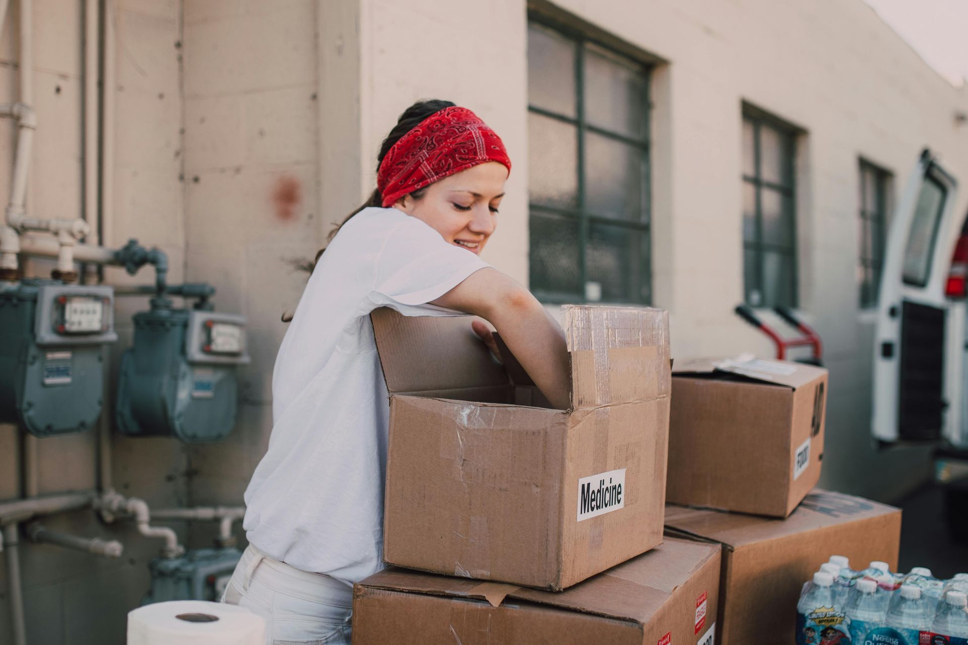 Woman in red headband packing boxes outdoors for charity.