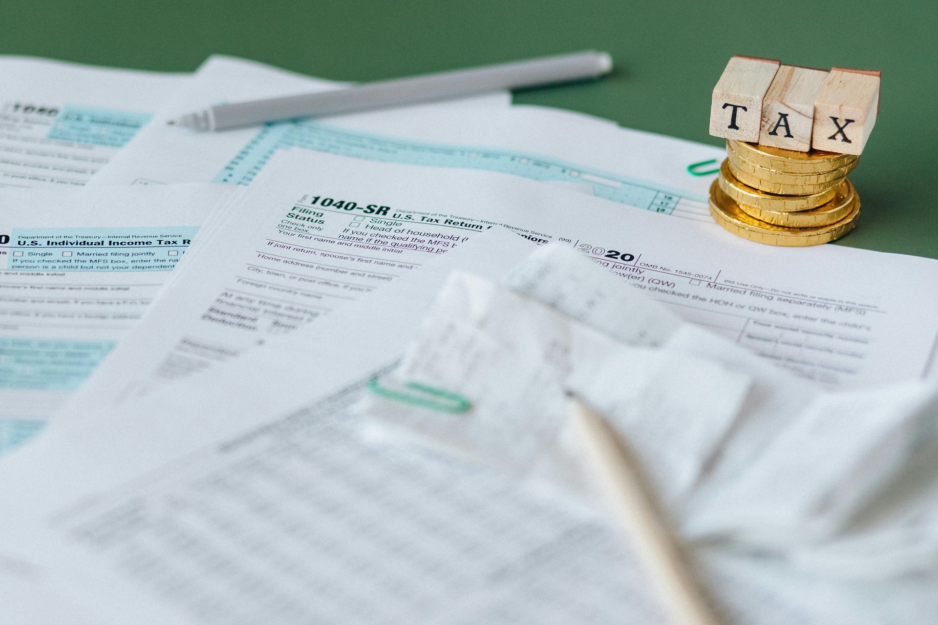 Tax papers with a calculator and pencil on a desk, plus stacked gold coins marked “TAX”