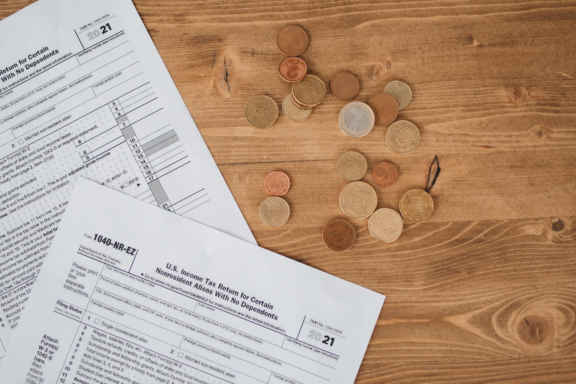Tax forms and scattered coins on a wooden surface.
