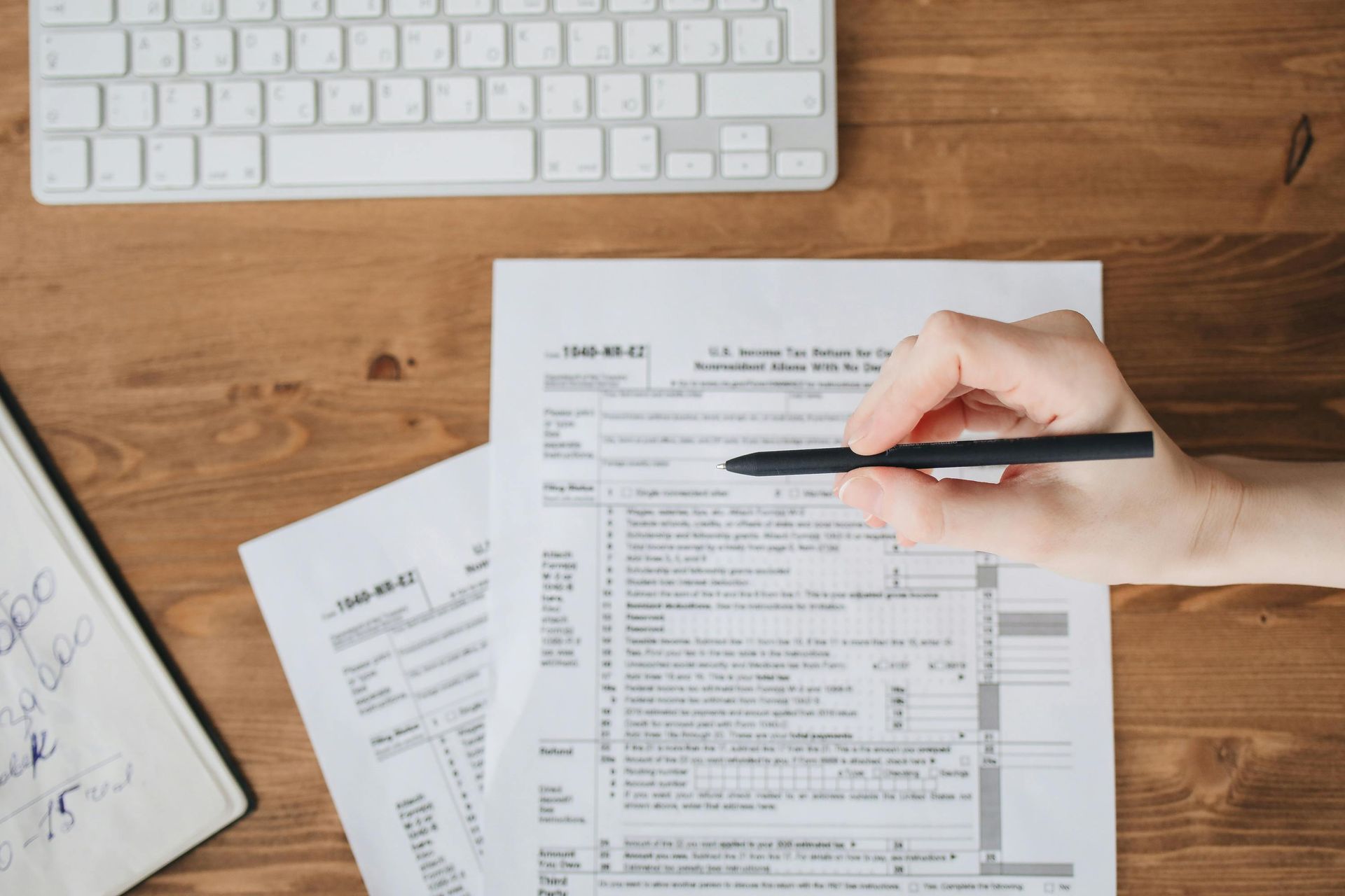 Hand writing on paperwork at a desk with keyboard and calculator nearby