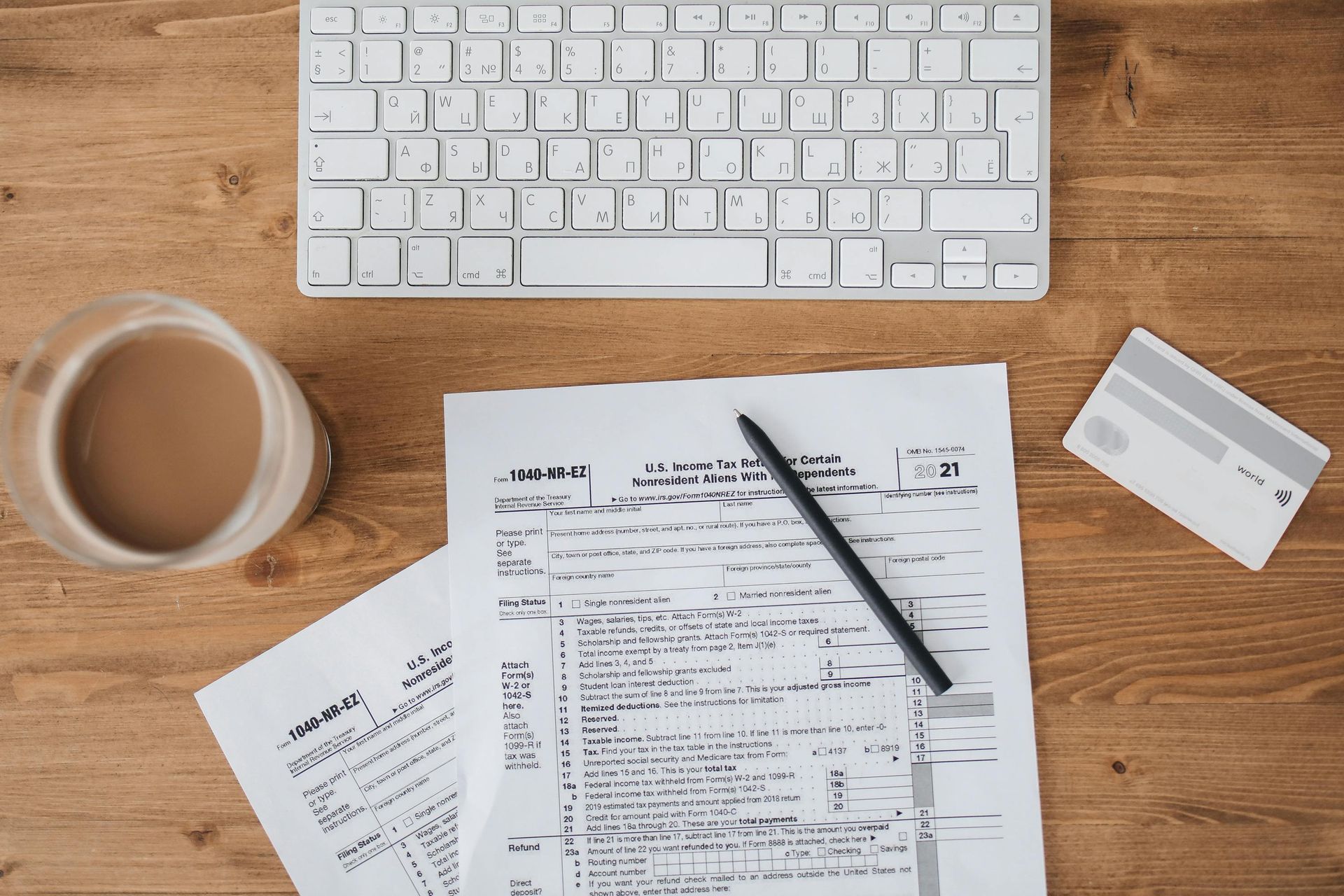 Keyboard, paperwork, pencil, credit card, and coffee on a wooden desk.