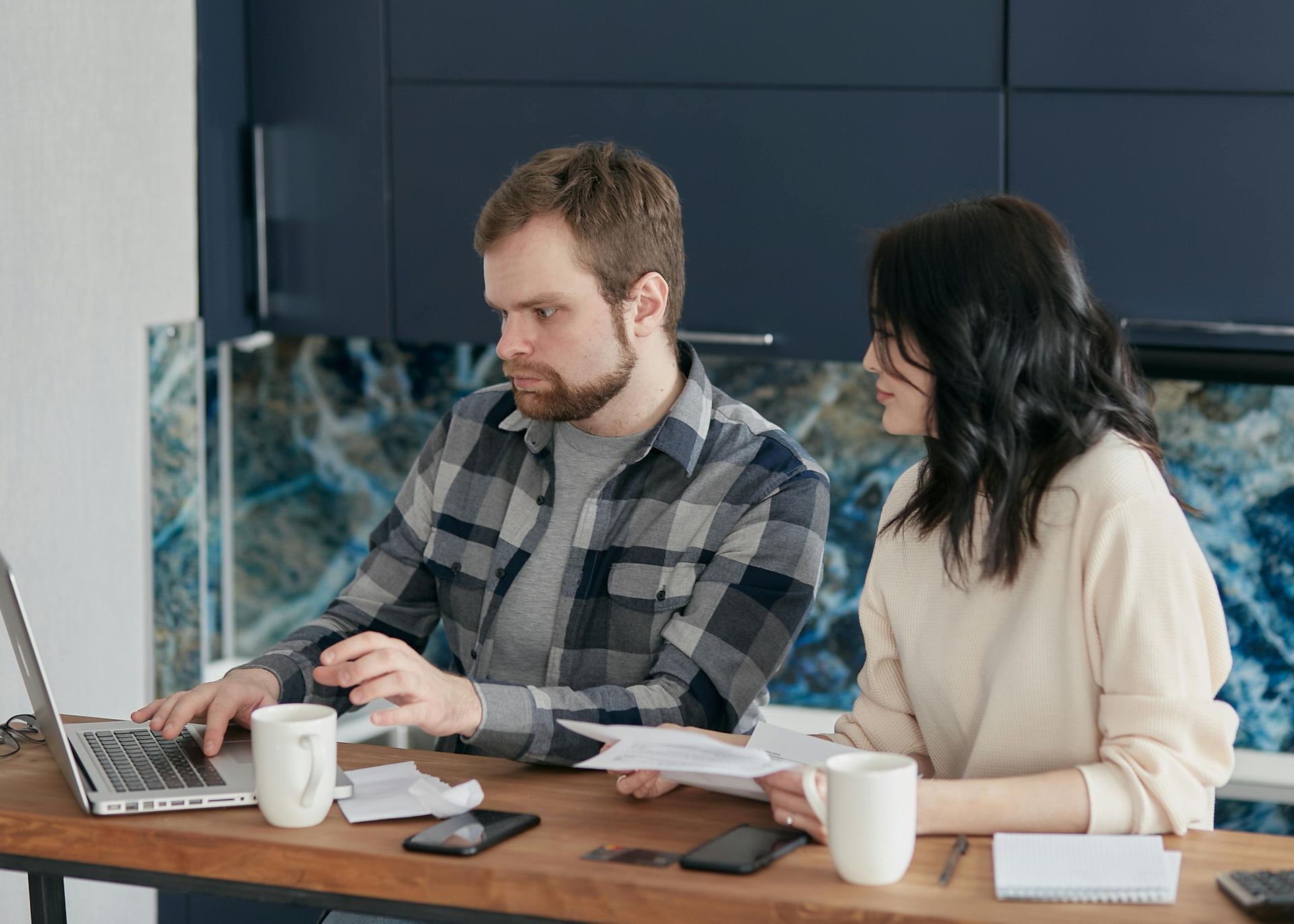 A man and a woman are sitting at a table looking at a laptop.