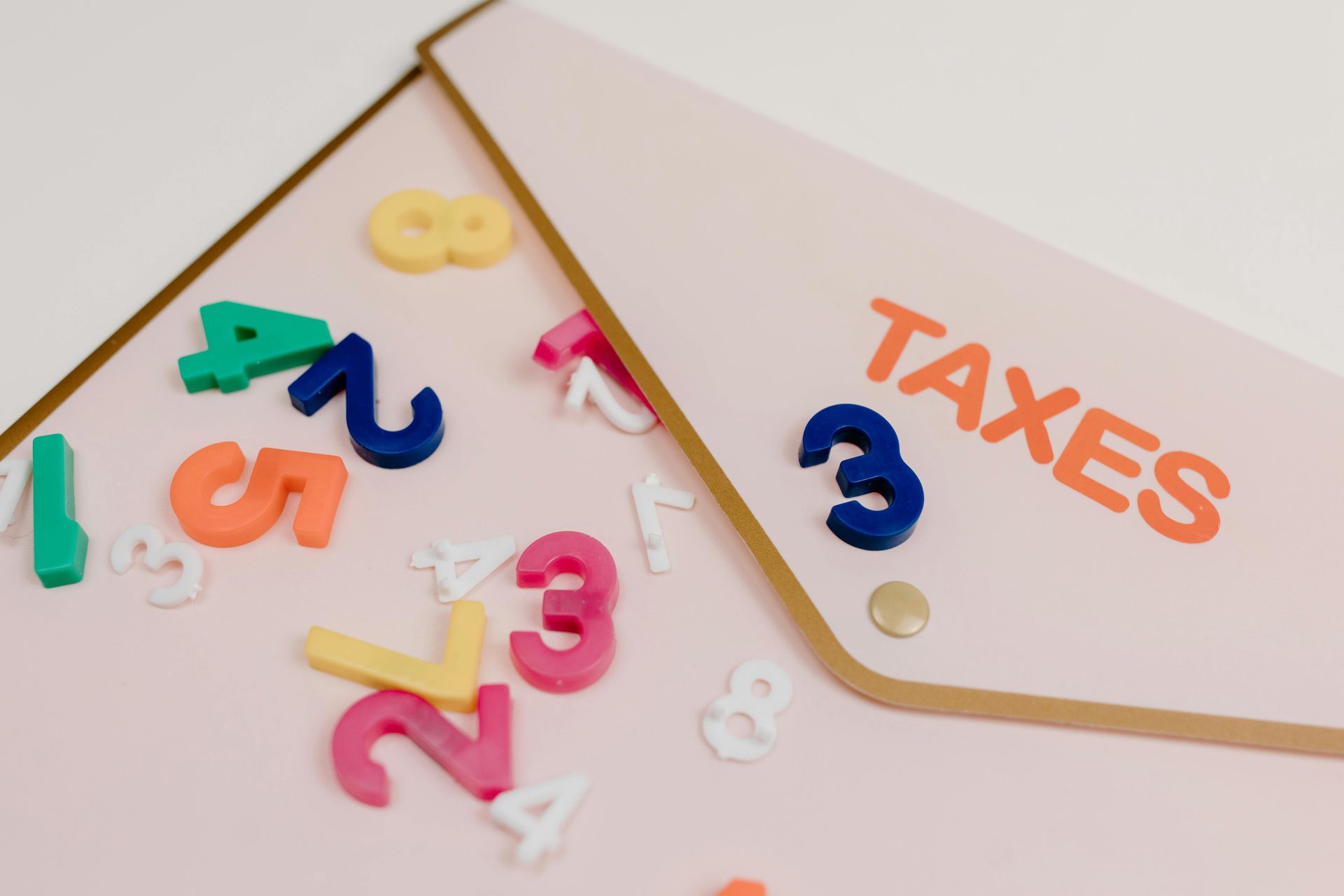 Colorful plastic letters and numbers around an envelope labeled “TAXES” on a pink background