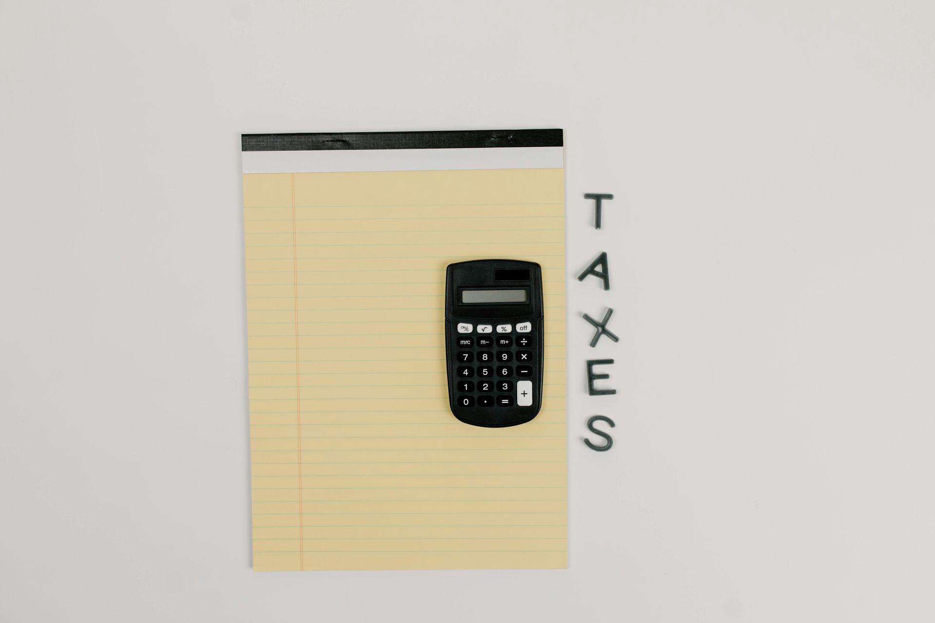 A black calculator sits on a yellow legal pad, with the word 