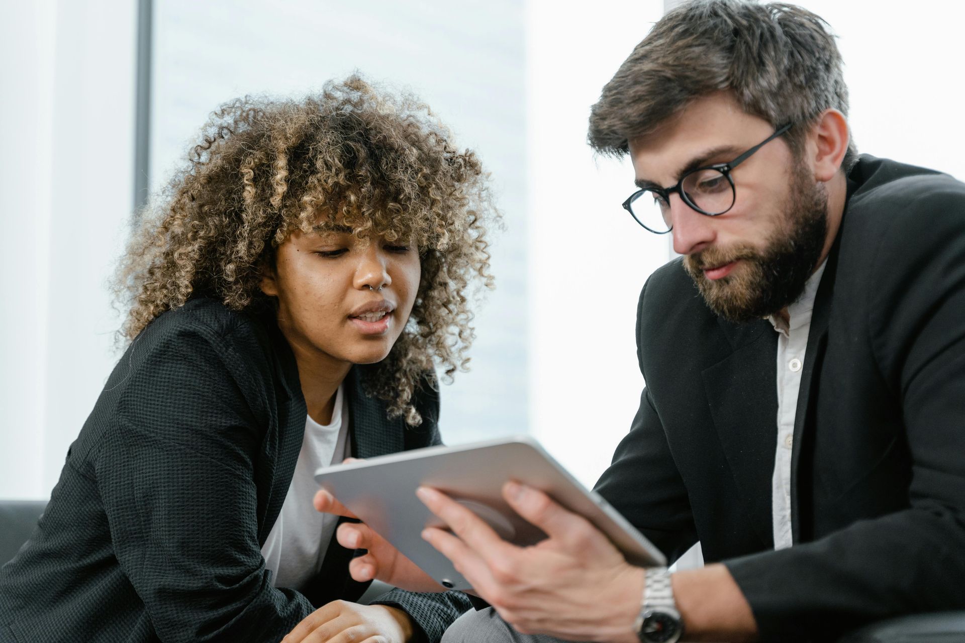 Woman and man in business attire looking at a tablet; indoors.