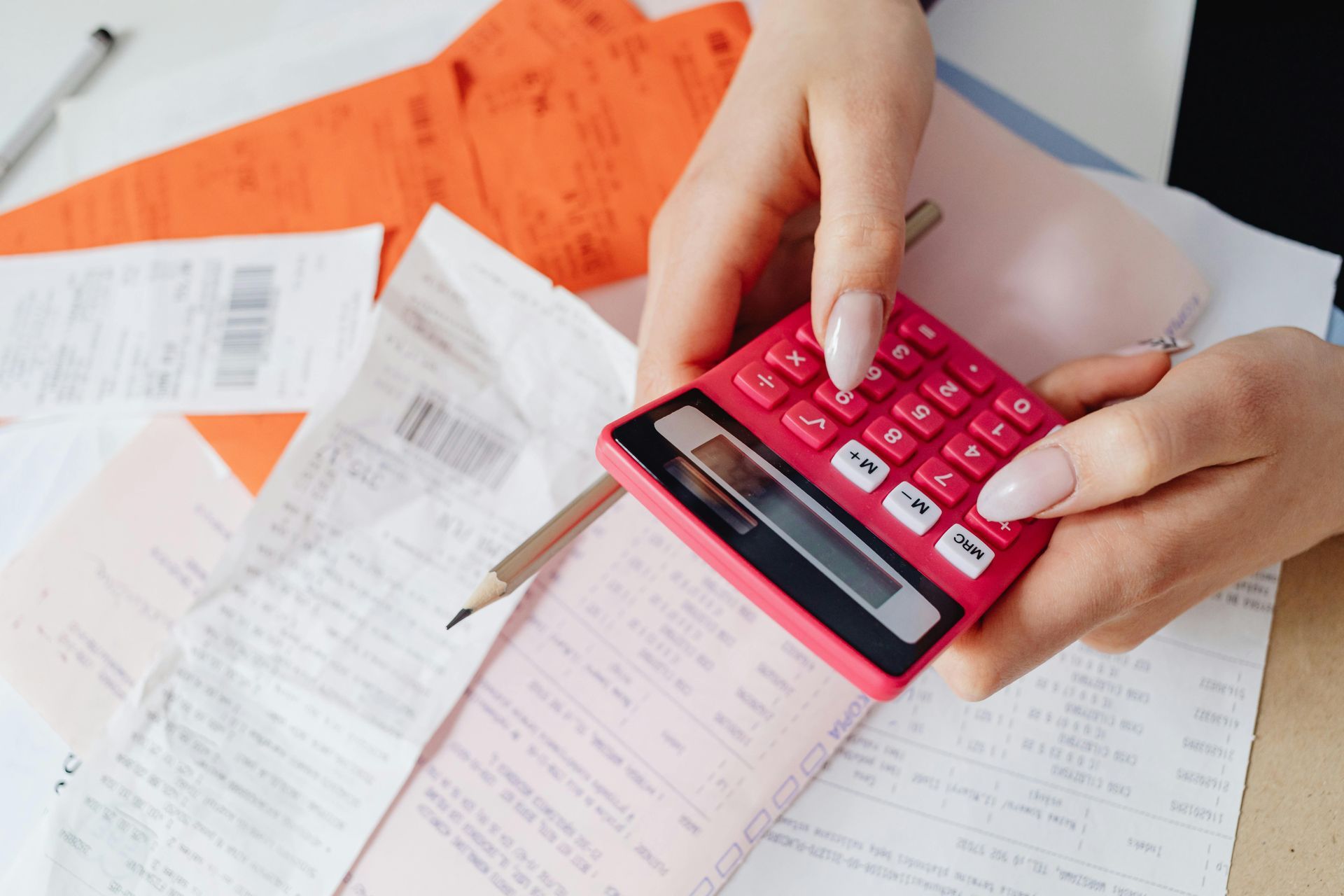 Hands holding a pink calculator, surrounded by receipts and a pencil.