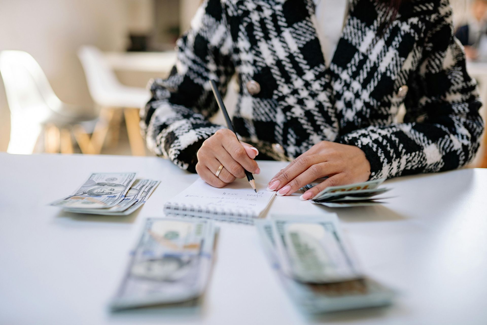 Person writing in a notebook at a table with stacks of US dollar bills.