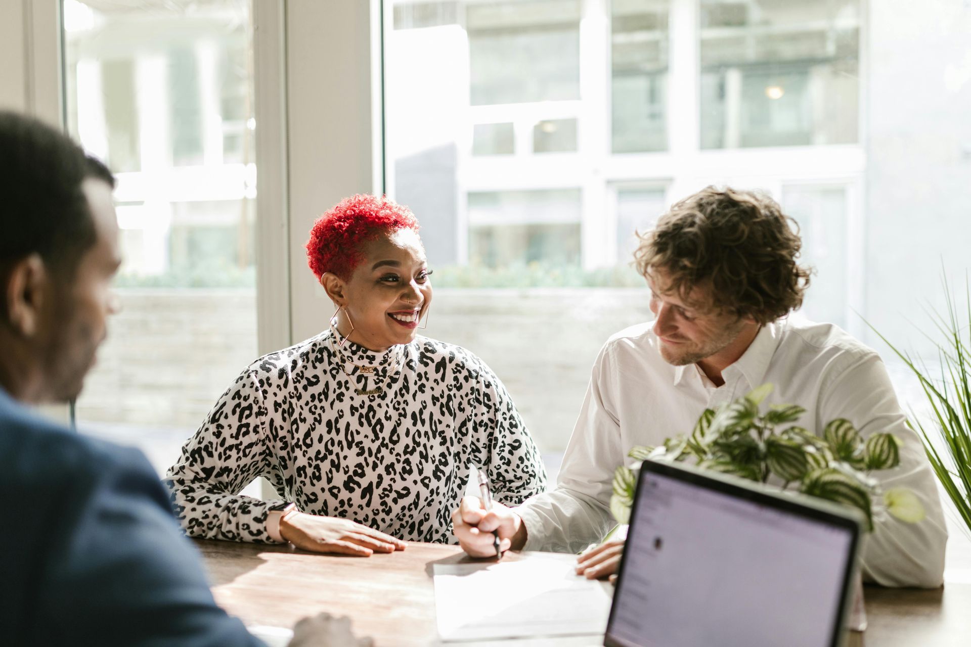 Three people in a meeting: Black woman with red hair smiles at a white man.