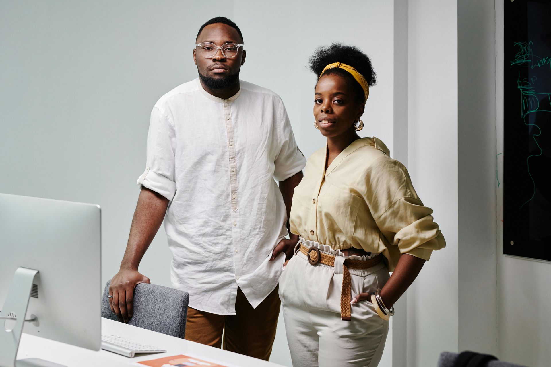 Two people standing in a modern office beside a desk and computer monitor.