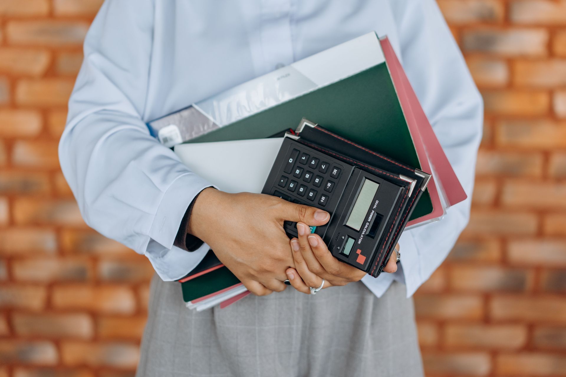 Person holding notebooks and a calculator against a plain background
