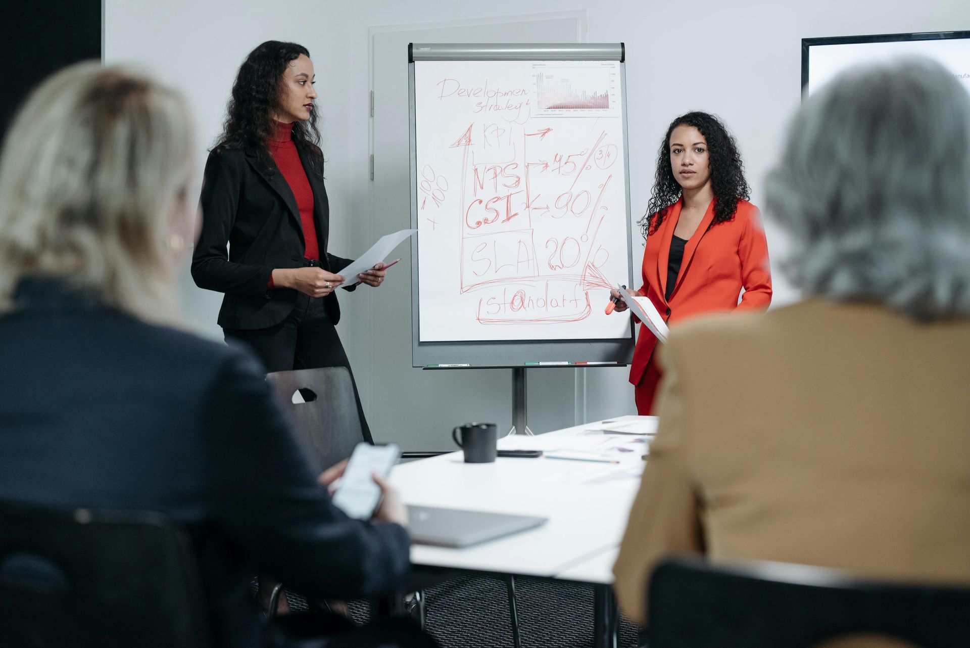 Two women are giving a presentation to a group of people in a conference room.