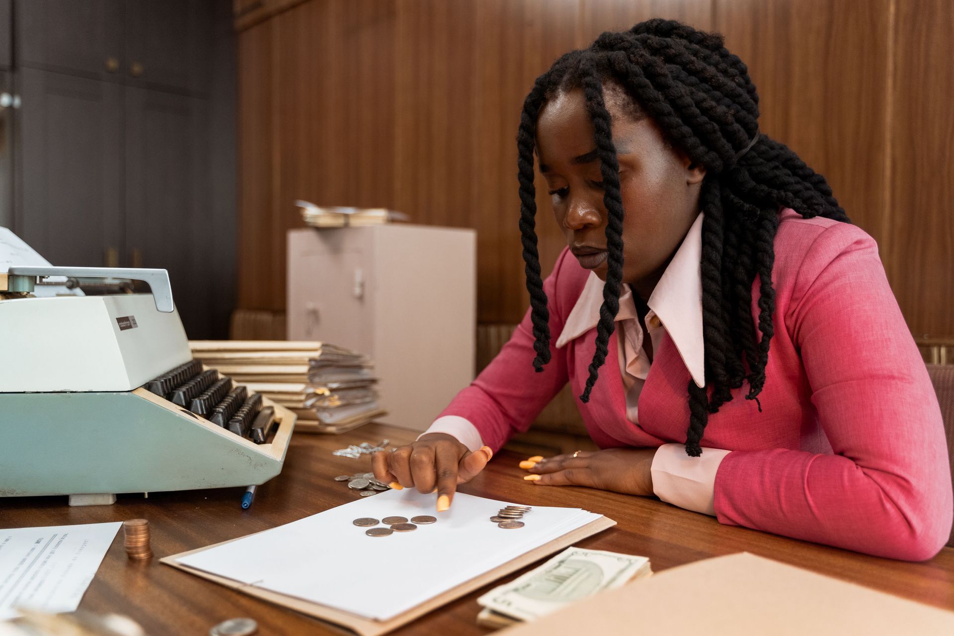 Person writing on a document at a desk beside a typewriter in an office
