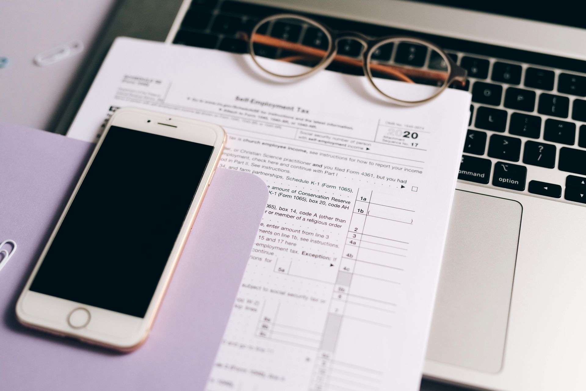 Smartphone on papers beside a laptop and glasses on a desk