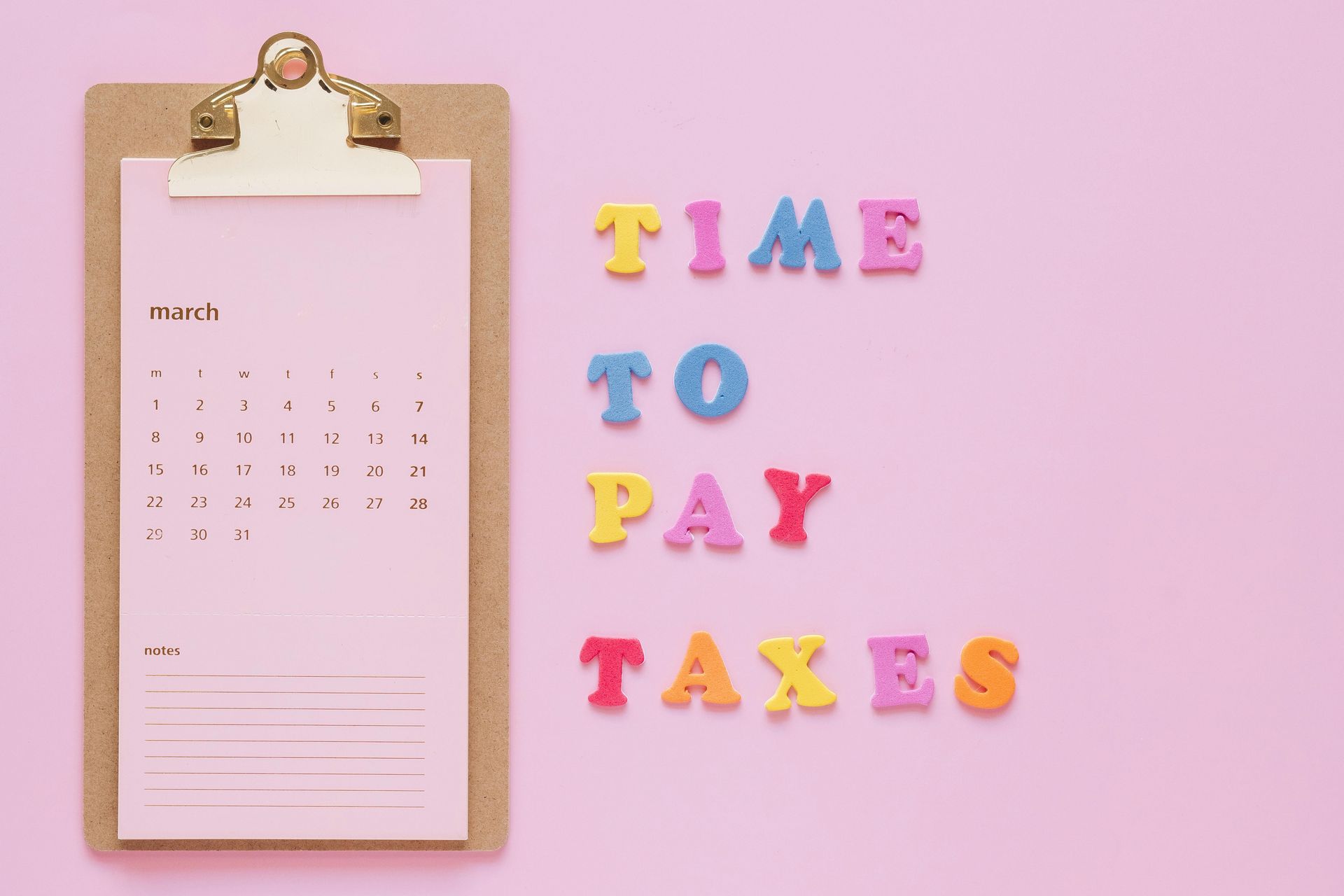 Clipboard calendar beside colorful letters spelling “TIME TO PAY TAXES” on a pink background
